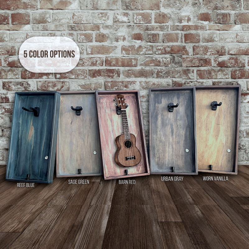 Five wooden ukulele cases in different colors displayed against a brick wall.