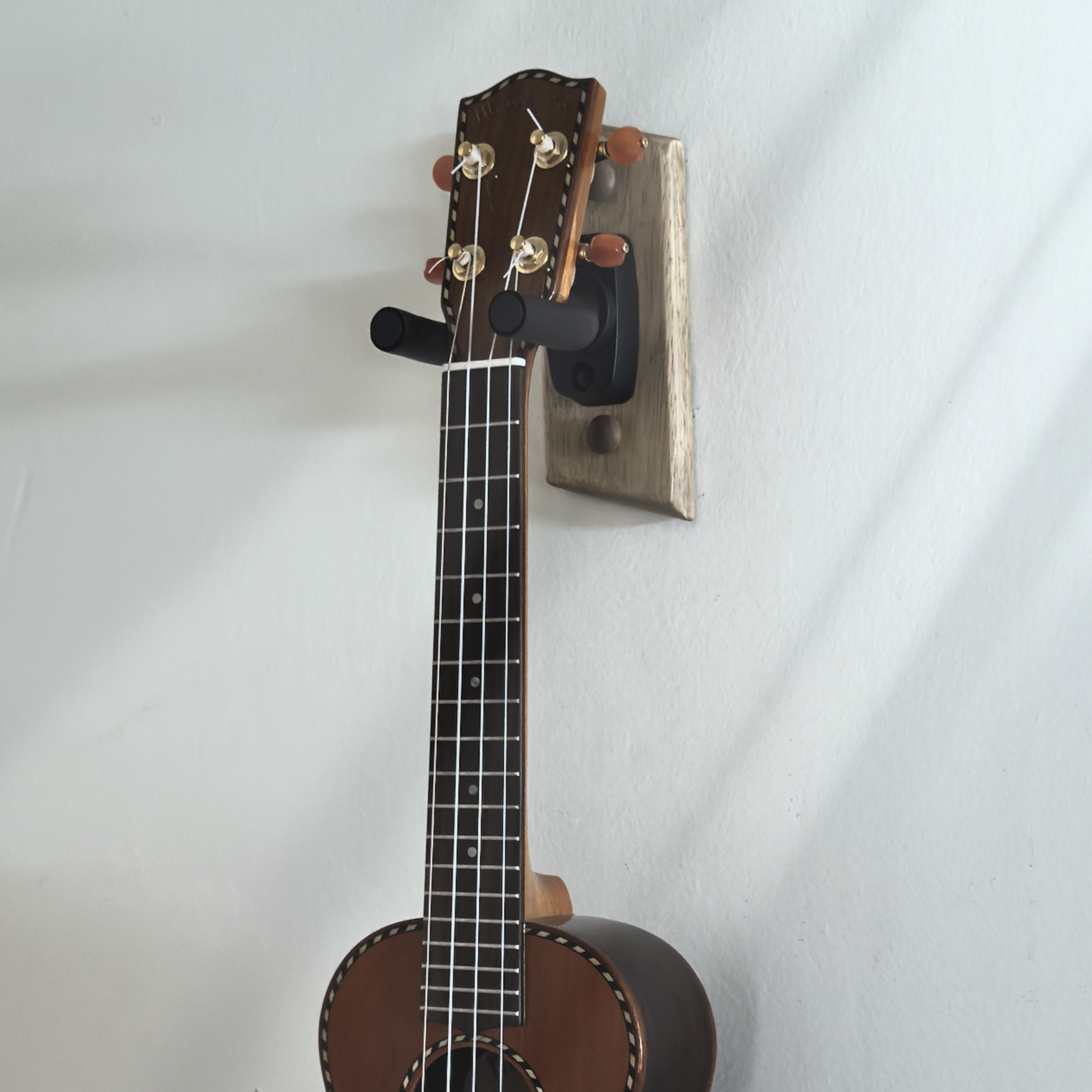 Handmade guitar wall hanger mounted on wall displaying concert size ukulele